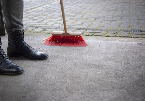 gehwegreinigung Mann mit Besen fegt Gehweg